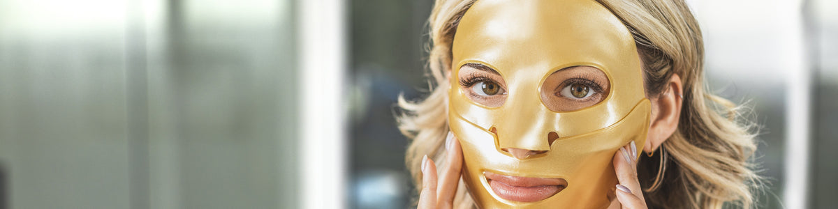 A woman wearing a KNESKO Gold Repair Collagen Face Mask, holding it gently against her cheeks.