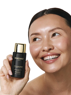 Woman holding a Knesko skincare product against a white background