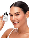 A smiling woman with dark hair pulled back holds up a small Knesko skincare dropper bottle against a clean white background.