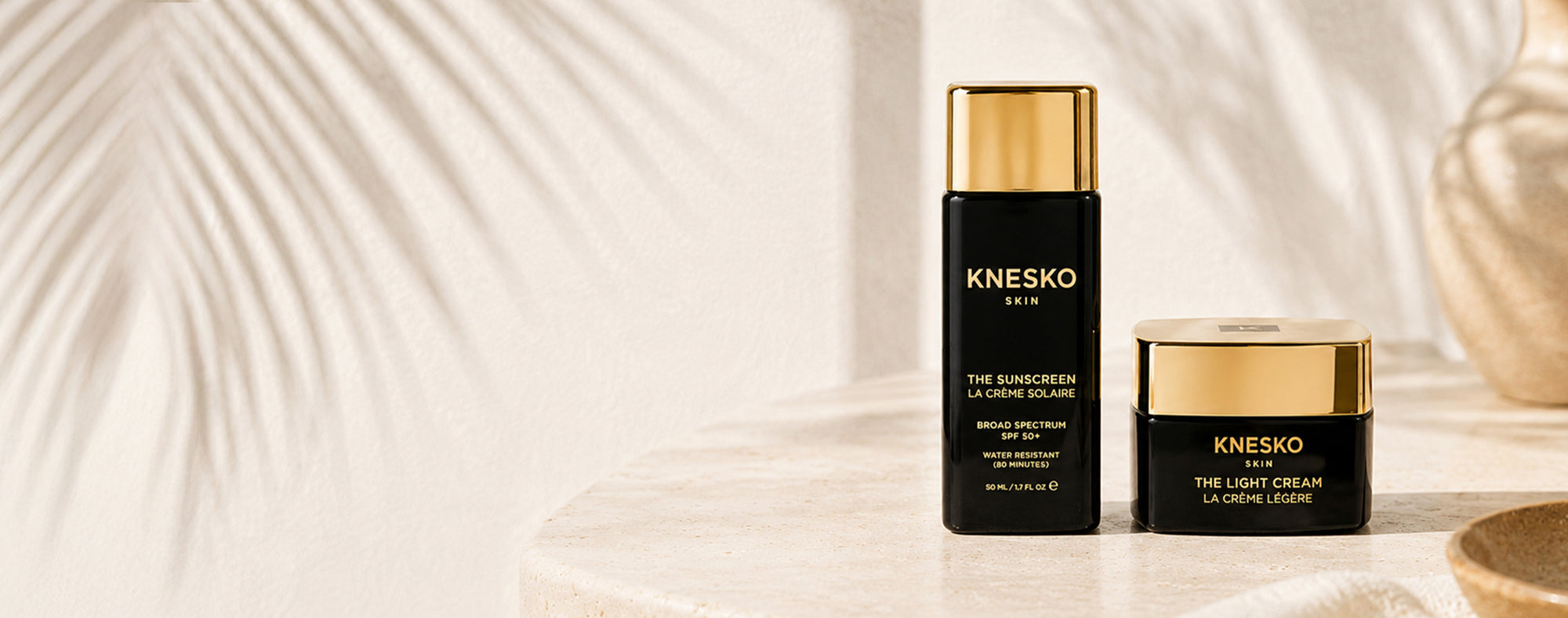 KNESKO Sunscreen bottle and Light Cream displayed on a light stone table.