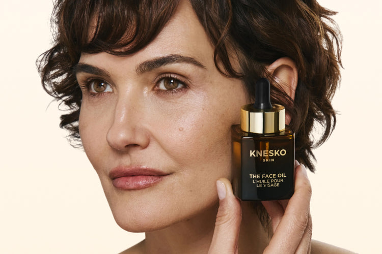 Woman holding a bottle of Knesko face oil close to her face.