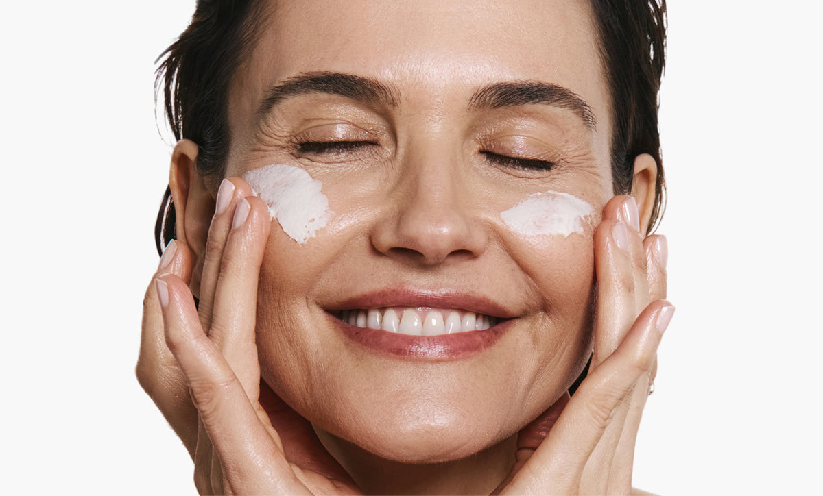 Woman applying skincare product on her face on white background