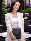 Woman holding a black clutch in an outdoor setting with greenery and pink flowers.