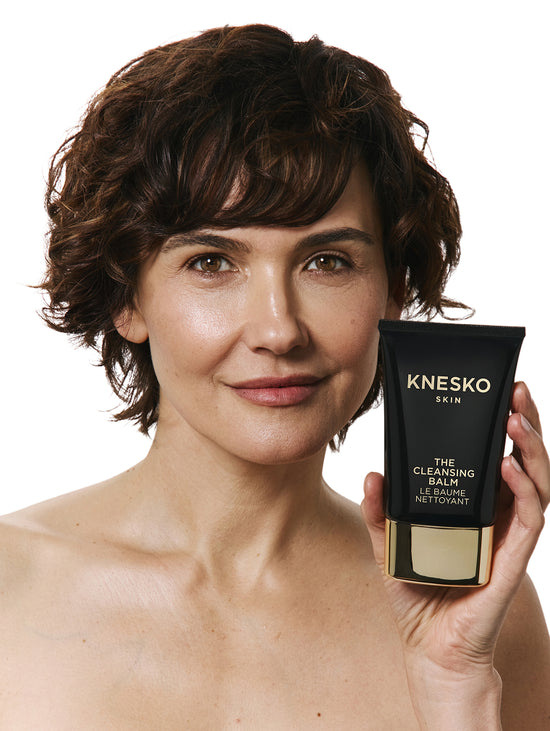 Woman holding a KNESKO cleansing balm bottle against a white background