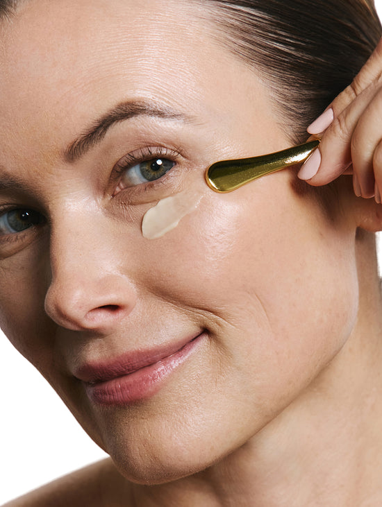 Woman applying eye cream with a applicator on a white background