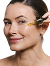 Woman applying the face oil with a dropper against a white background