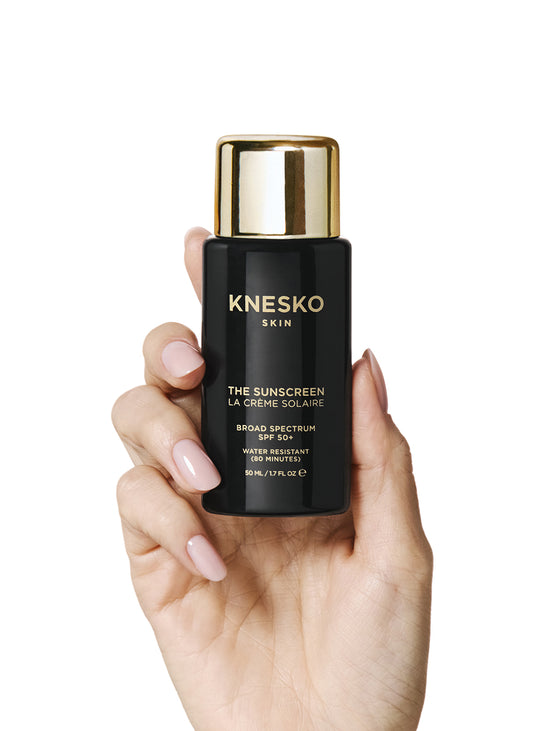 Hand holding a Knesko skincare product on a white background