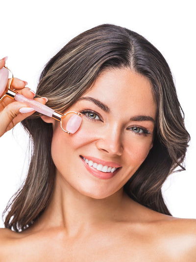 Woman using a pink face roller on her face against a white background