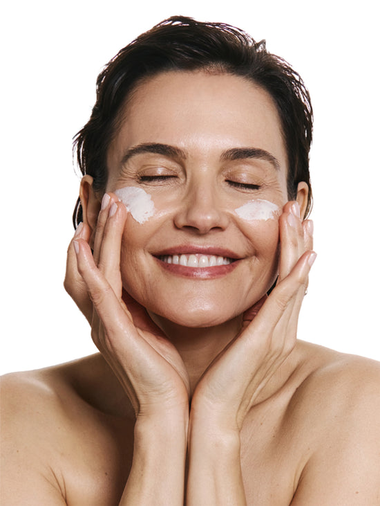 Woman applying product to her face with a white background