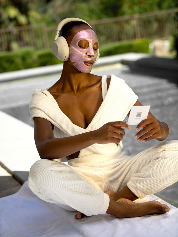 Woman masking and meditating, holding a KNESKO meditation card with headphones