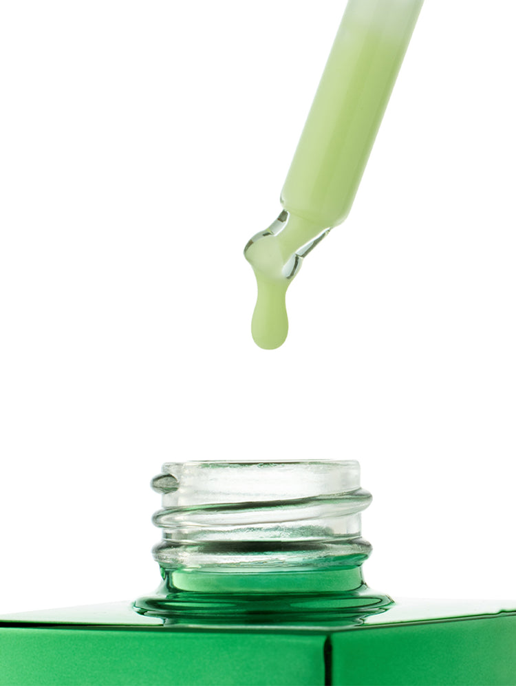A close-up studio shot of a clear glass dropper holding a pale green liquid, with a single drop hanging above an open green bottle on a white background.