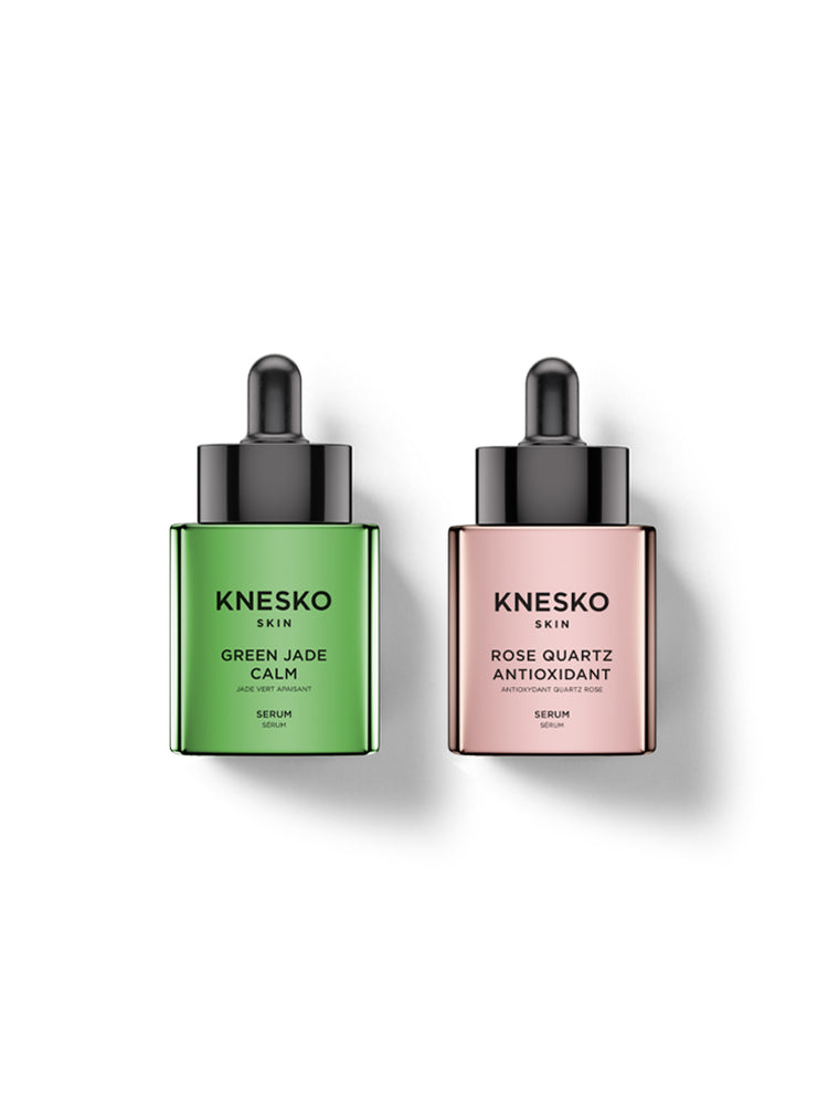 Two Knesko Skin serum bottles on a white background, one in green labeled Green Jade Calm and one in pink labeled Rose Quartz Antioxidant.
