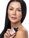 A woman with long black hair holds an Avene Hyaluve White-Celadon Serum bottle against a clean white background.