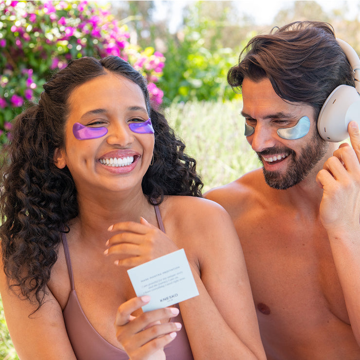 Two people outdoors with eye masks on, one holding a card.