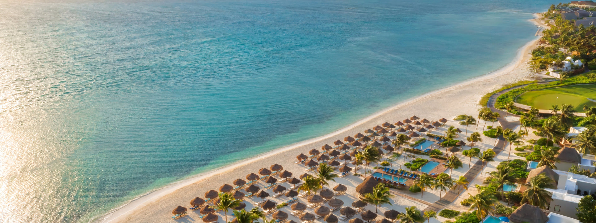 Aerial view of a tropical beach with a resort and clear blue water.