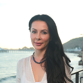 Woman with long dark hair standing outdoors with a scenic background