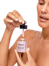 A close-up of a woman holding a pink Knesko Rose Quartz Antioxidant serum bottle and dropper against a clean white background.