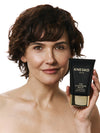 Woman holding a KNESKO cleansing balm bottle against a white background