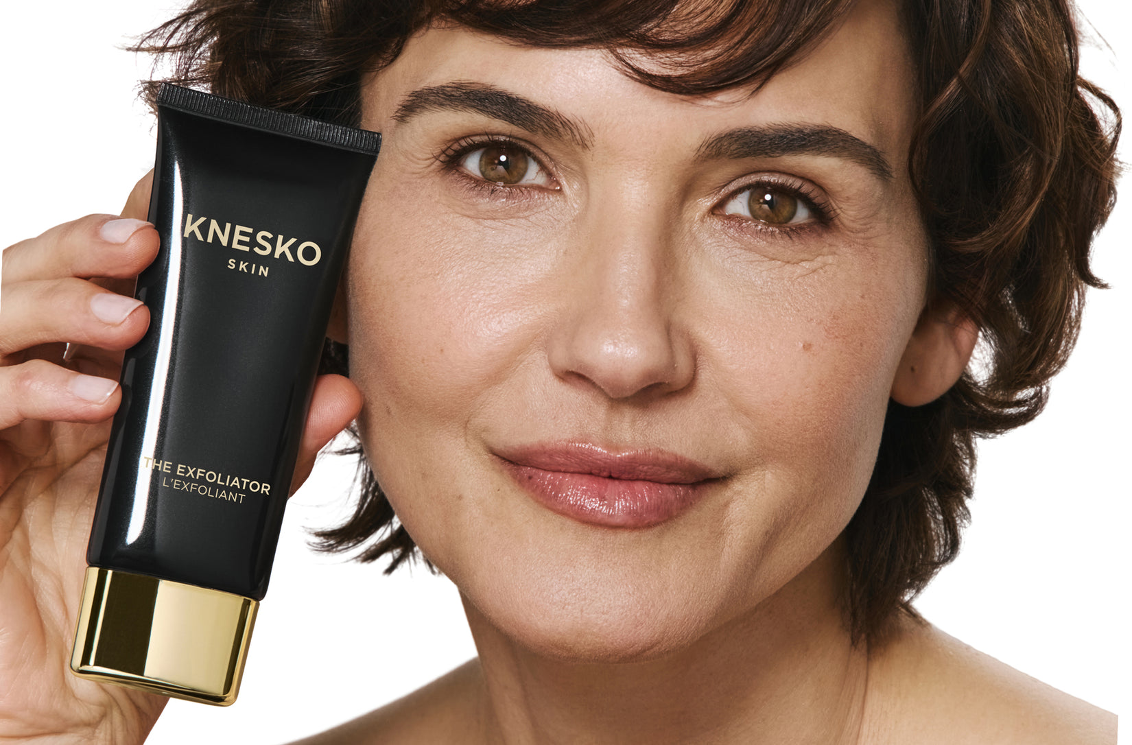 Woman holding a Knesko skincare product against a white background