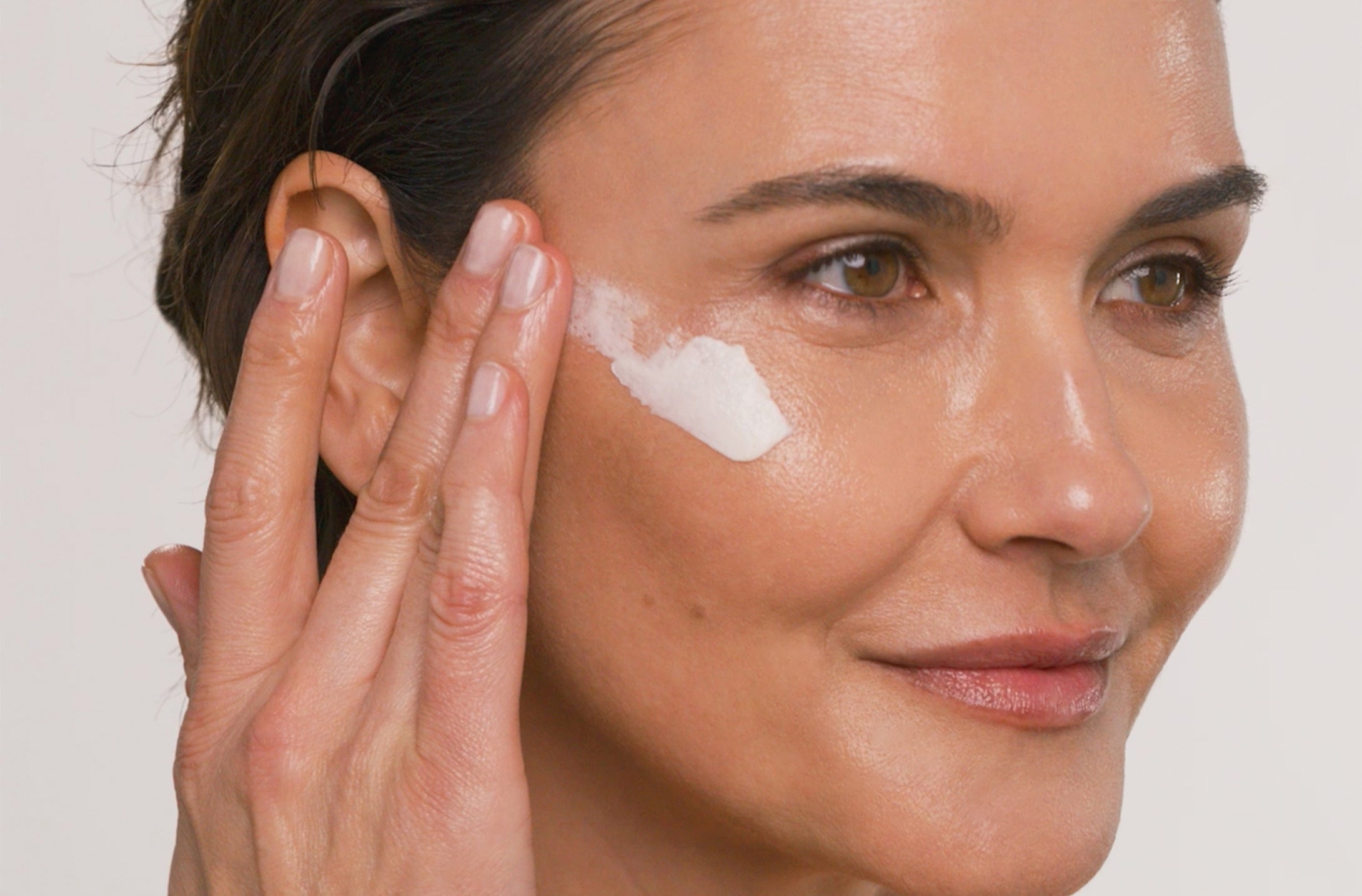 Woman applying product to her face with a neutral background
