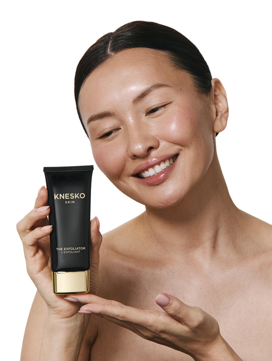 Woman holding KNESKO exfoliator bottle against a white background