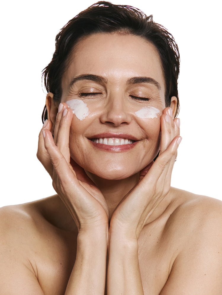 Woman applying product to her face with both hands against a white background