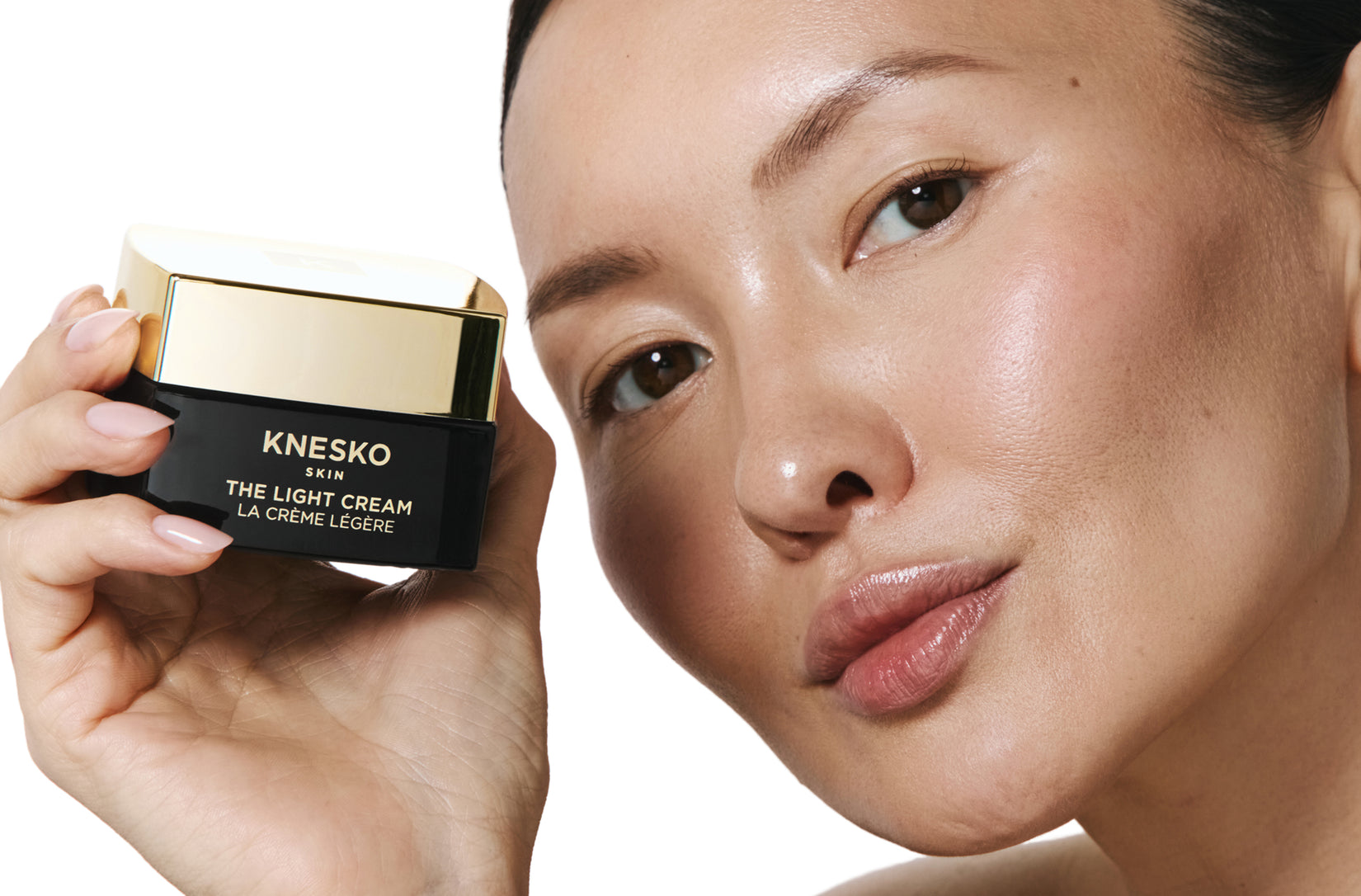 Person holding a Knesko skincare product with a close-up of their face.