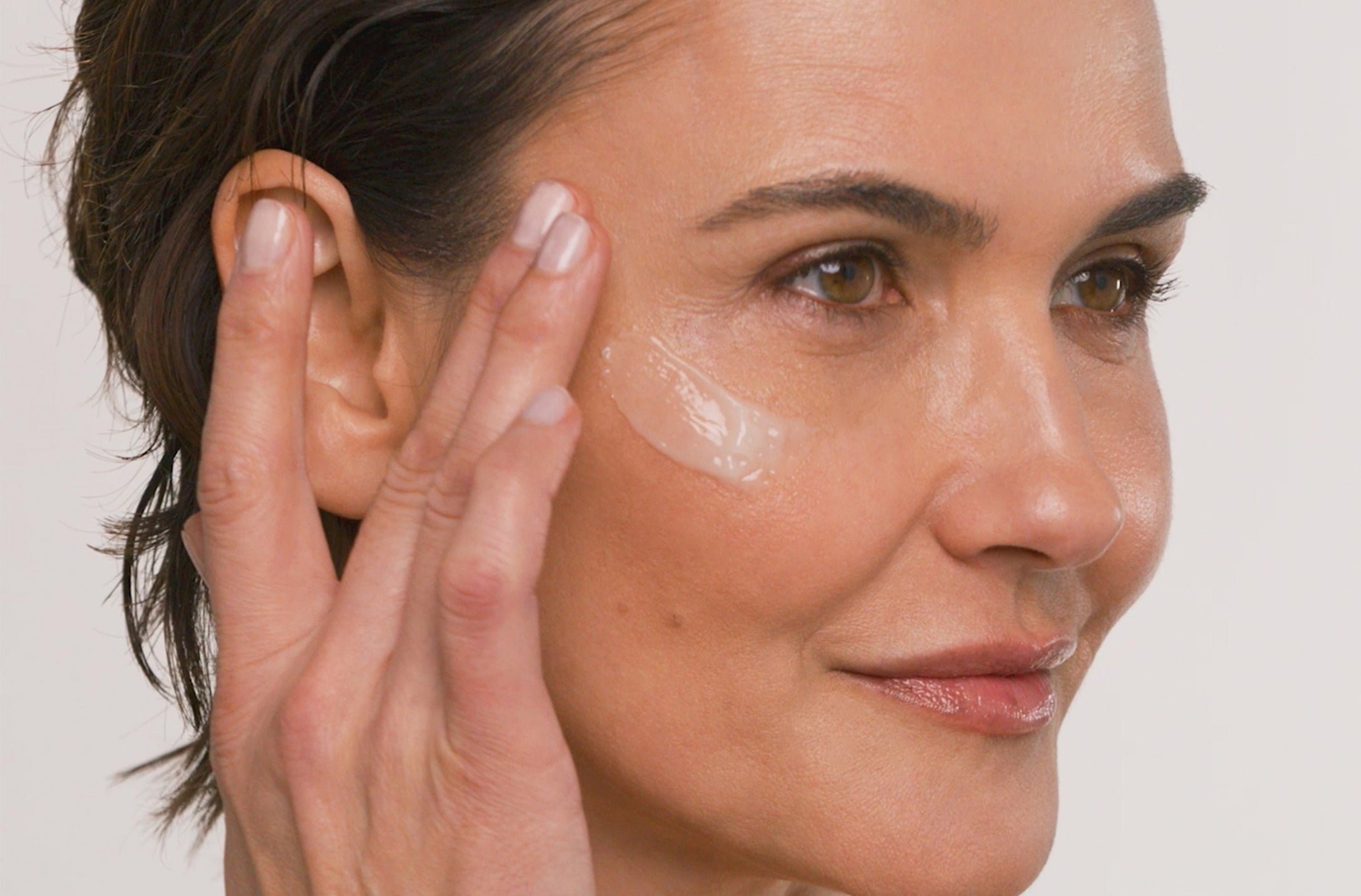 Woman applying product to her face with a neutral background