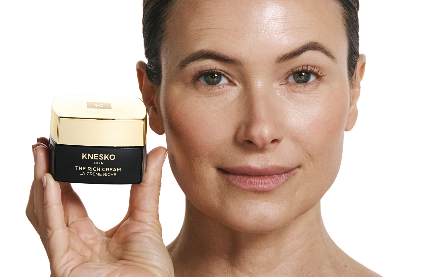 Woman holding a container of Knesko cream against a white background