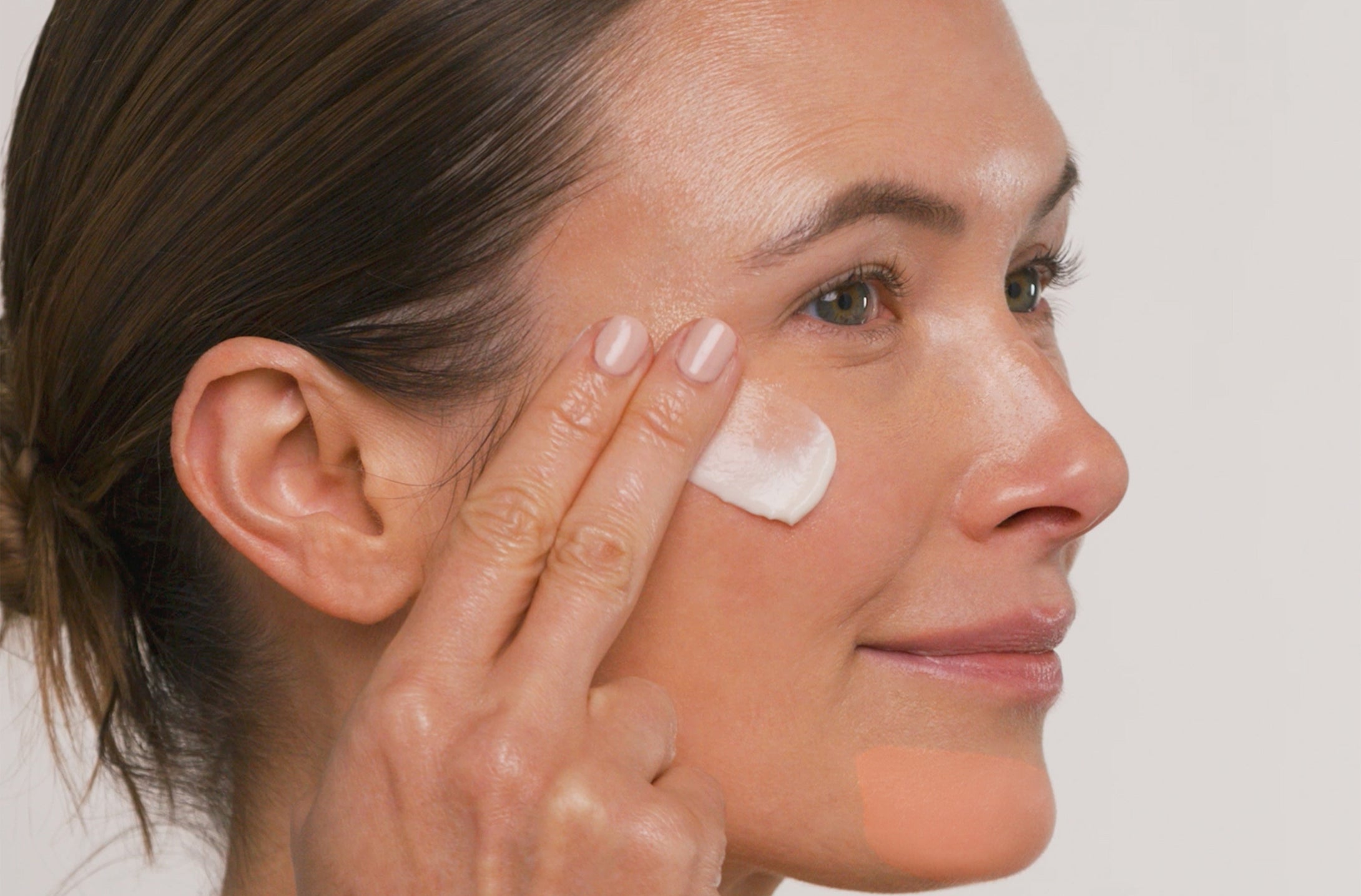Woman applying cream to her face with a neutral background