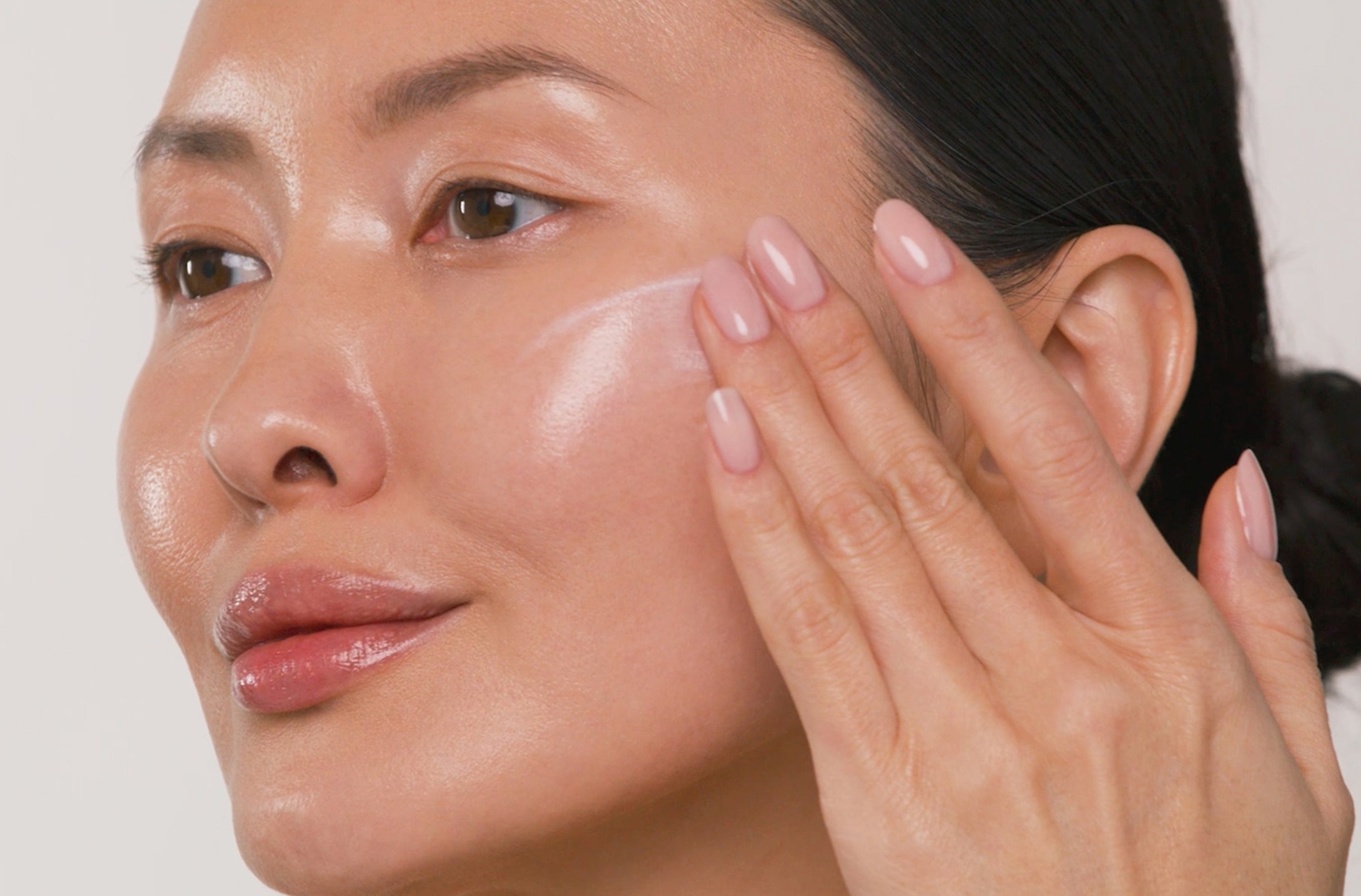 Woman applying cream to her face with a neutral background